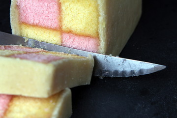 Freshly cut Battenberg Cake on dark slate background with knife. Pink and yellow sponge covered in marzipan