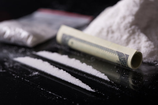 Rolled hundred dollars banknote, two lines and pile of cocaine o