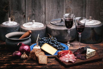 Meat and cheese appetizers selection on a rough old wood background with grapes, two glasses of wine and pottery