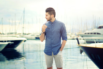 Portrait of young bearded handsome man with luxury yachts in port.
