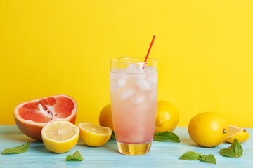 Glass of pink lemonade and citrus on turquoise table and yellow background