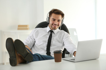 Handsome man listening to music with headphones and putting feet at table