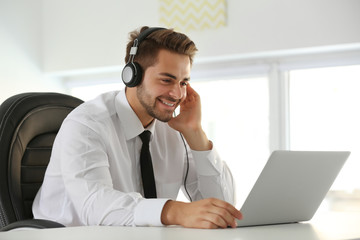 Handsome young man listening to music with headphones and working on laptop at office