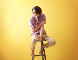Handsome young man sitting on stool on yellow background