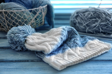 Knitted cap with yarn and metal basket on wooden background