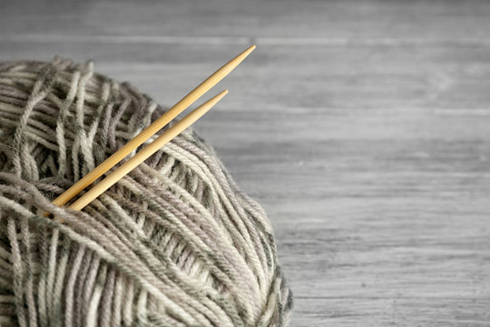 Ball of multicolored knitting yarn and needles on grey wooden background