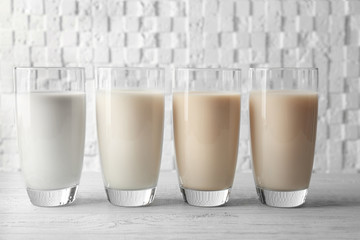 Glasses of almond, rice, sesame and coconut milk on wooden table against white blurred background