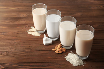 Glasses of almond, rice, sesame and coconut milk on wooden table