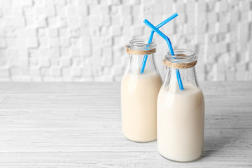 Two bottles of tasty milk with straws on wooden table against white blurred background