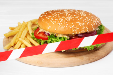 Tasty hamburger and french fries crossed with warning tape. Diet concept