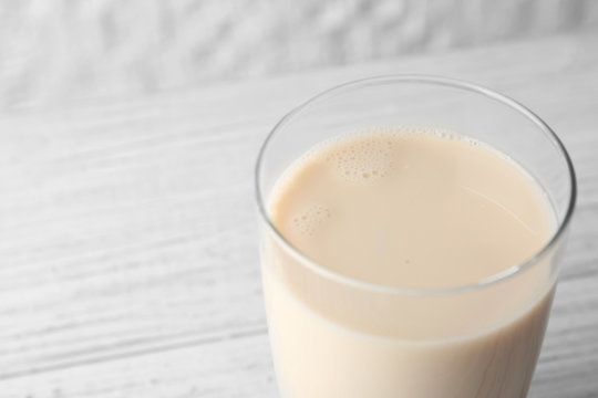 Glass of tasty milk on white wooden table, close up view