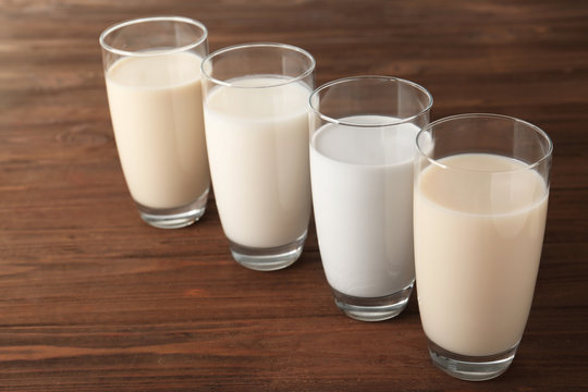 Glasses of almond, rice, sesame and coconut milk on wooden table