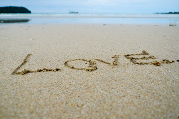 Fototapeta na wymiar Abstract sign of word love written on a sand beach background