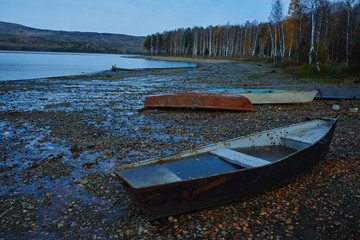 Boats lie on the stony shore of the pond on the background of forest and mountains