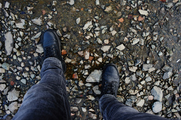 The view from the top, feet in jeans and leather shoes standing on the stony shore