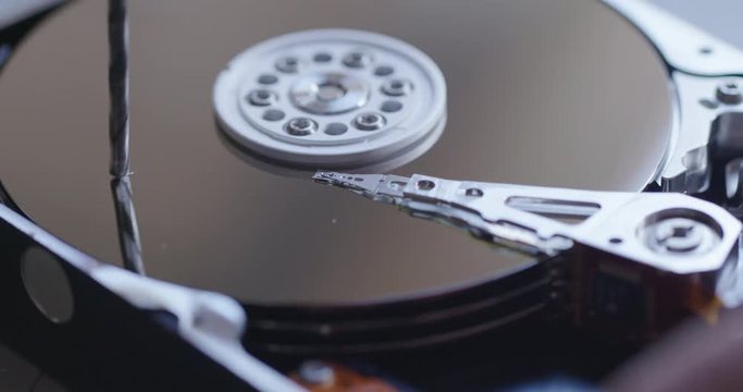 Close up view of an electric drill and its reflection as it destroys a computer hard drive by creating a physical hole.  Macro shot.