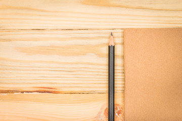 Brown note book with pencil on wood background