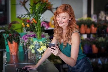 Female florist using mobile phone while using laptop