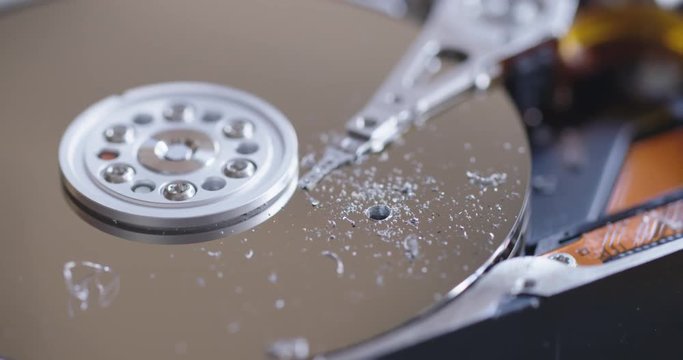 Pan to a view of a hole drilled through a computer hard drive and surrounding debris.  Macro shot.
