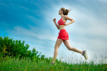 Young lady running. Woman runner running through the summer park rural road. Workout in a park. Beautiful fit girl. Fitness model caucasian ethnicity outdoors. Weight loss exercise. Jogging.