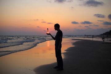 Man holds the electric light bulb and the sun on the beach at sunset