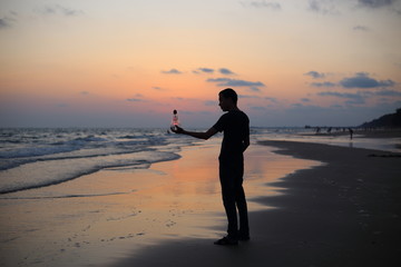 Man holds the electric light bulb and the sun on the beach at sunset