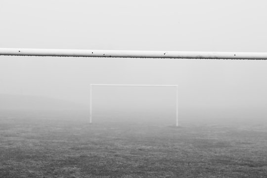 Black and white image of soccer football goal posts in empty field pitch in winter fog