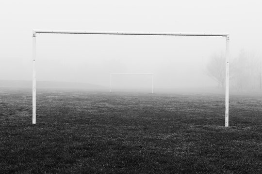 Black and white image of soccer football goal posts in empty field pitch in winter fog