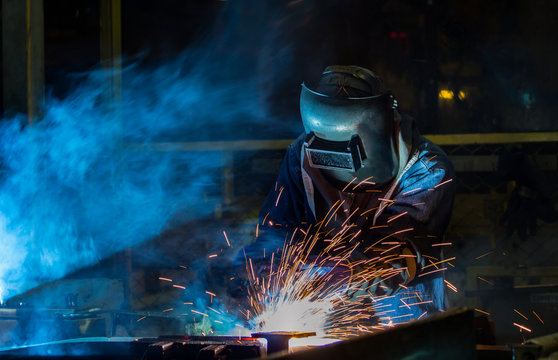 Worker with protective mask welding automotive part in factory