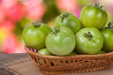 unripe green tomatoes in a wicker basket on  wooden table with  blurred background