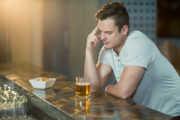 Thoughtful man with glass of whisky sitting at bar counter