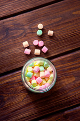 Multicolored marshmallows in the glass jar on a wooden board.