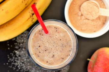 Healthy fresh smoothie drink from red apple, banana chia seeds and plant protein powder in the glass with straw