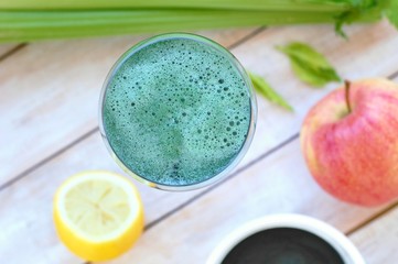 Healthy fresh smoothie drink from red apple, green algae spirulina, lemon, and celery in the glass on wooden background