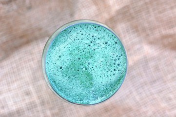 Healthy fresh smoothie drink from red apple, green algae spirulina, lemon, and celery in the glass on brown background