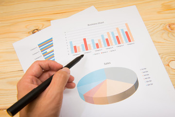 Businessman's hand showing diagram on financial report with pen.