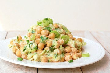 Healthy meal from chickpeas, zucchini, spring onion and cream on white plate on wooden background