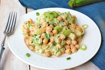 Healthy meal from chickpeas, zucchini, spring onion and cream on white plate on wooden background