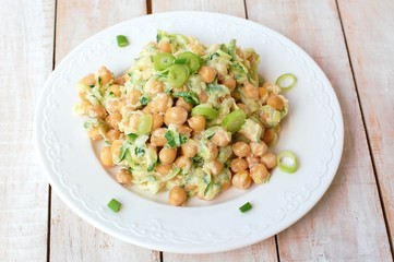 Healthy meal from chickpeas, zucchini, spring onion and cream on white plate on wooden background