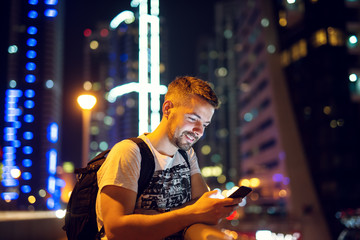 Young man in big city looking at smart phone and typing.