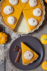 Thanksgiving homemade pumpkin pie with whipped cream and spices on rustic background, top view. Autumn Decoration and rustic style.