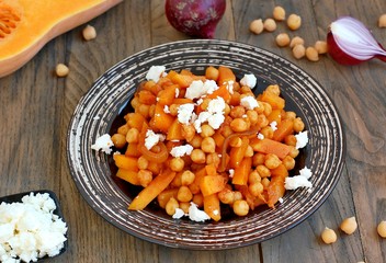 Healthy meal from chickpeas, pumpkin, red onion and cheese on white plate on dark wooden background