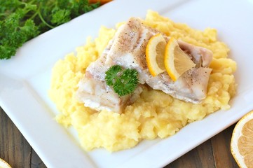Healthy meal from fish and mashed potatoes with lemon and parsley on white plate on dark brown wooden background