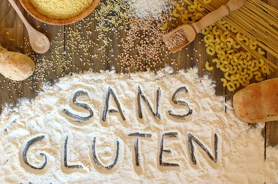 Gluten free cereals corn, rice, buckwheat, quinoa, millet, pasta and flour with text gluten free in French language on brown wooden background