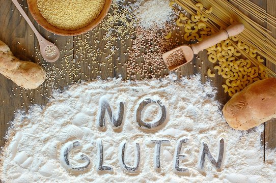 Gluten free cereals corn, rice, buckwheat, quinoa, millet, pasta and flour with scratched text no gluten on brown wooden background