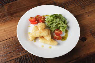 Breaded cheese (deep-fry) with tomatoes and greens in a white plate. Wooden background