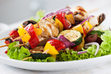 Closeup of chicken skewers or shashlik with grilled vegetables (mushrooms, paprika, salad, zucchini, onion).