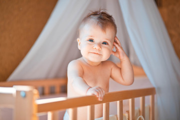 incredibly beautiful and cute little girl stands in crib