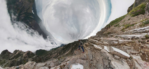 A man stands in the mountains and looks into the distance, above