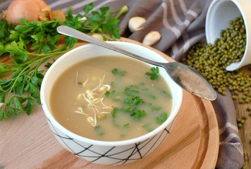 Healthy vegan soup from mung bean, coriander, garlic and onion in bowl on wooden background